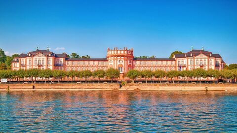 Das Schloss Biebrich gehört zu den bedeutendsten Barockbauwerke am Mittelrhein.  Im Wasser des Rheins spiegelt sich das Barockschloss Schloss Biebrich, das im Hintergund zu sehen ist..