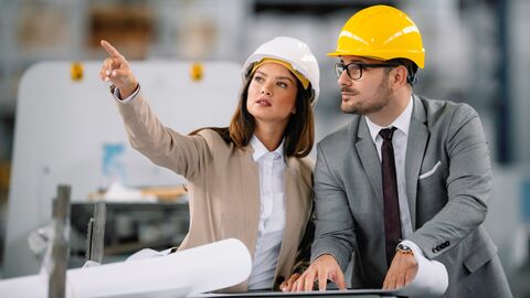 Architektin und Architekt prüfen einen Bauplan und diskutieren über ihre Arbeit