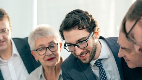Mit der Zentralen Vergabe erfüllt der LBIH die hohen Anforderungen an Zuverlässigkeit und Rechtssicherheit bei öffentlichen Ausschreibungen. Nahansicht: Lächelnde Teammitglieder diskutieren in einem Büro