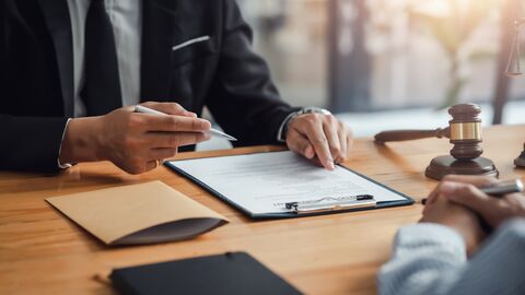 Der LBIH vermarktet seit 2005 Liegenschaften aus Fiskalerbschaften. Im Bild sind die Hände von zwei Personen zu sehen, die sich an einem Tisch gegenübersitzen. Der Mann im Anzug sitzt links im Bild und zeigt auf einen Vertrag. Neben ihm liegt ein Richterhammer. Die Person rechts im Bild hält einen Stift in den Händen.