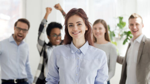 Lächelnde junge Frau im Vordergrund mit mehreren Personen im Hintergrund, die sich freuen