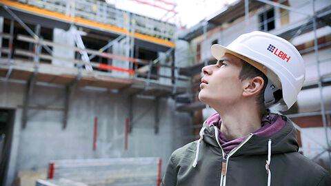 Im Vordergrund steht ein Auszubildender des LBIH und schaut auf eine Baustelle, die im Hintergrund zu sehen ist. 