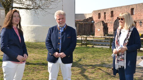 Drei Personen auf einer Wiese vor Gebäuden