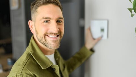 Energie sparen Ein Mann lächelt in die Kamera und reguliert dabei die Heizung.