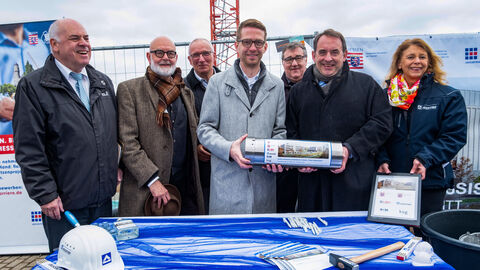 Von links nach rechts zu sehen sind Thomas Platte (Direktor Landesbetrieb Bau und Immobilien Hessen), Professor Johannes Kister (Gesellschafter kister scheithauer gross architekten und stadtplaner GmbH), Hartmut Römer (Direktor Landesbetrieb Hessisches Landeslabor), Michael Ruhl (Staatssekretär im Hessischen Ministerium für Landwirtschaft und Umwelt), Mark Weinmeister (Regierungspräsident Kassel), Professor Dr. R. Alexander Lorz (Finanzminister) und Sandra Arendt (Niederlassungsleitung Soziale Infrastruktur Europa, HOCHTIEF PPP Solutions). Im Bild ist eine Gruppe von Vertretern aus Politik und dem Baubereich zu sehen. Sie halten eine Zeitkapsel in der Hand.