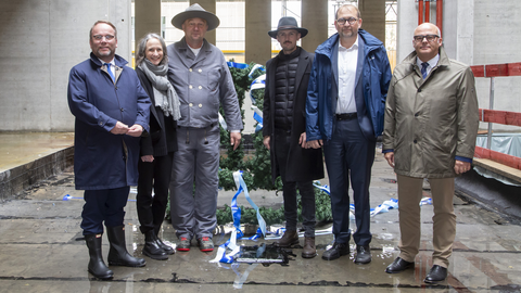 Von links nach rechts sind im Rohbau des neuen Gebäudes zu sehen: Hessens Wissenschaftsminister Timon Gremmels, Gabriele Schmücker-Winkelmann, Leiterin der Niederlassung Rhein-Main des LBIH, Oberpolier Peter Schulz, Polier Marko Kovacevic, Uni-Präsident Prof. Dr. Enrico Schleiff und Elmar Damm, Abteilungsleiter im Hessischen Finanzministerium. Zum Richtfest sind wichtige Personen aus Politik und Verwaltung erschienen. Sie stehen in einem Halbkreis im Rohbau und lächeln in die Kamera.